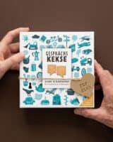 Zwei Hände halten die Schachtel Gesprächskekse mit türkisen Illustrationen, am Verschluss hängt ein Kraftpapier-Herz mit der Aufschrift für dich