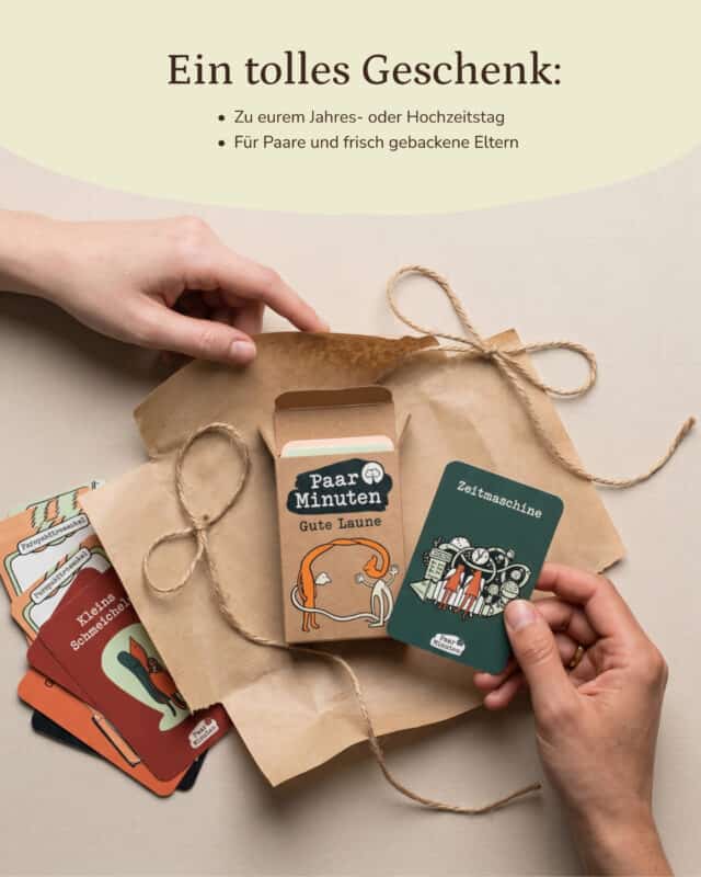 Zwei Hände verpacken die geöffnete Schachtel PaarMinuten Gute Laune in Kraftpapier mit Kordel, daneben liegen aufgefächerte Fragekarten und eine grüne Karte „Zeitmaschine“