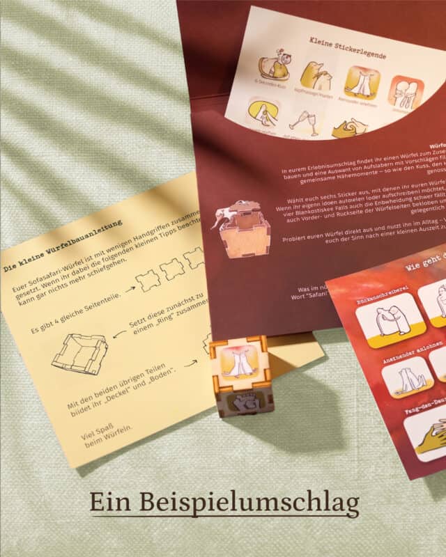 Aufgeklappter Erlebnisumschlag der Sofasafari mit Stickerlegende, Bogen „Die kleine Würfelbauanleitung“ und einem zusammengesteckten Holzwürfel mit aufgeklebten Symbolen